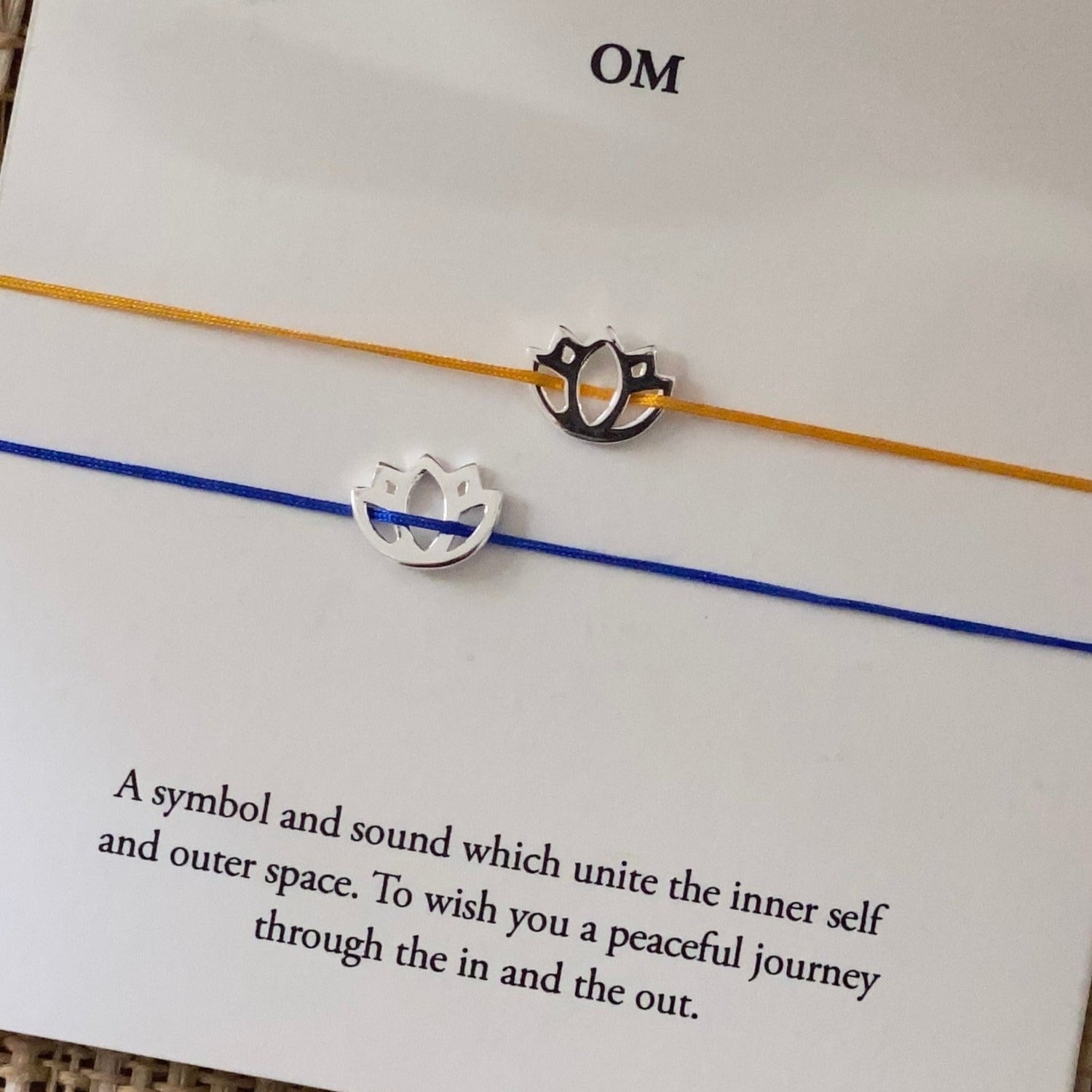 Yellow and blue cord lotus charm bracelets displayed on a meaning card