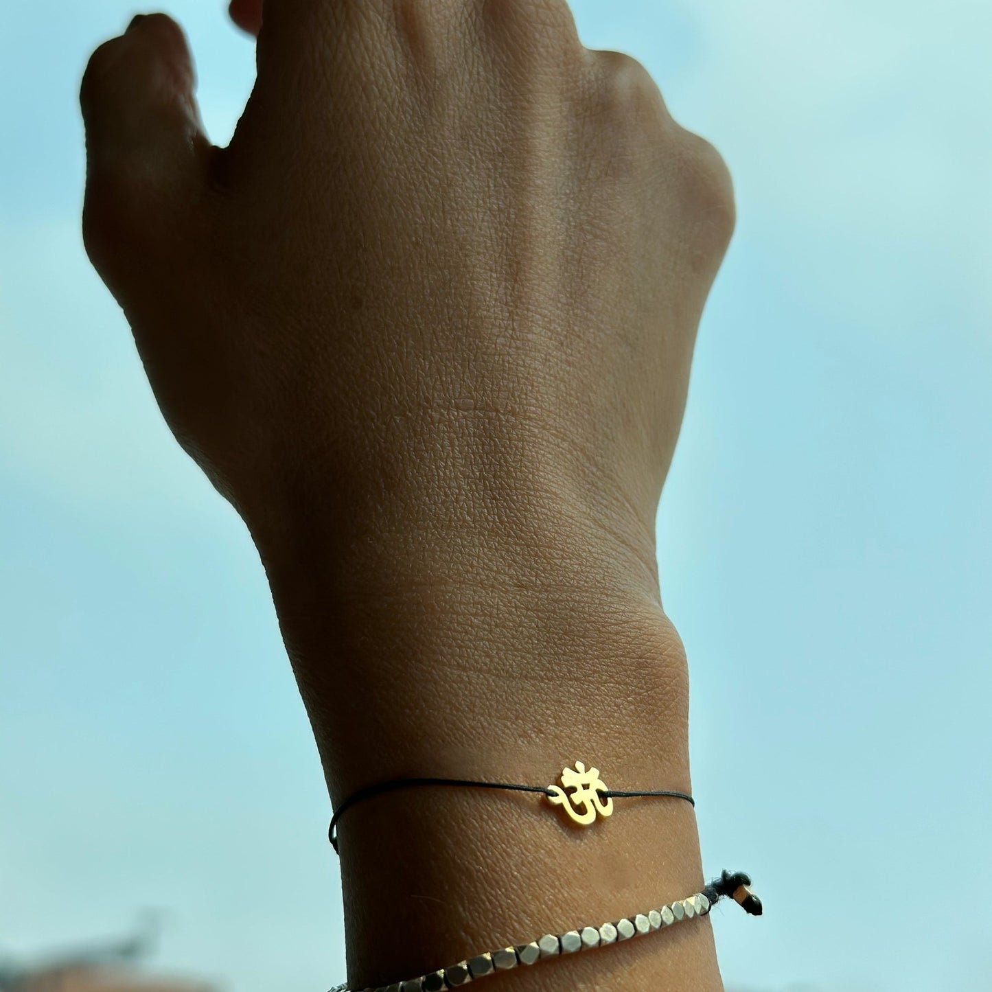 Wrist wearing a black cord OM charm bracelet with a beaded bracelet