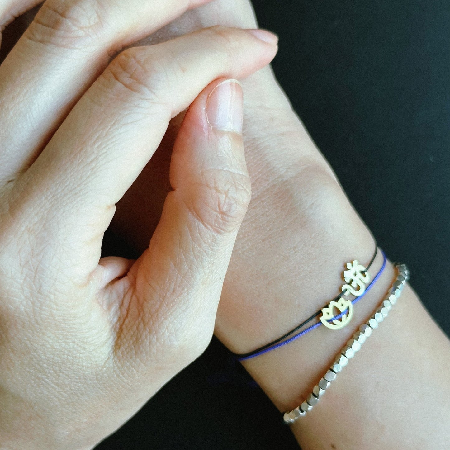 Wrist wearing a purple cord OM charm bracelet with a beaded bracelet