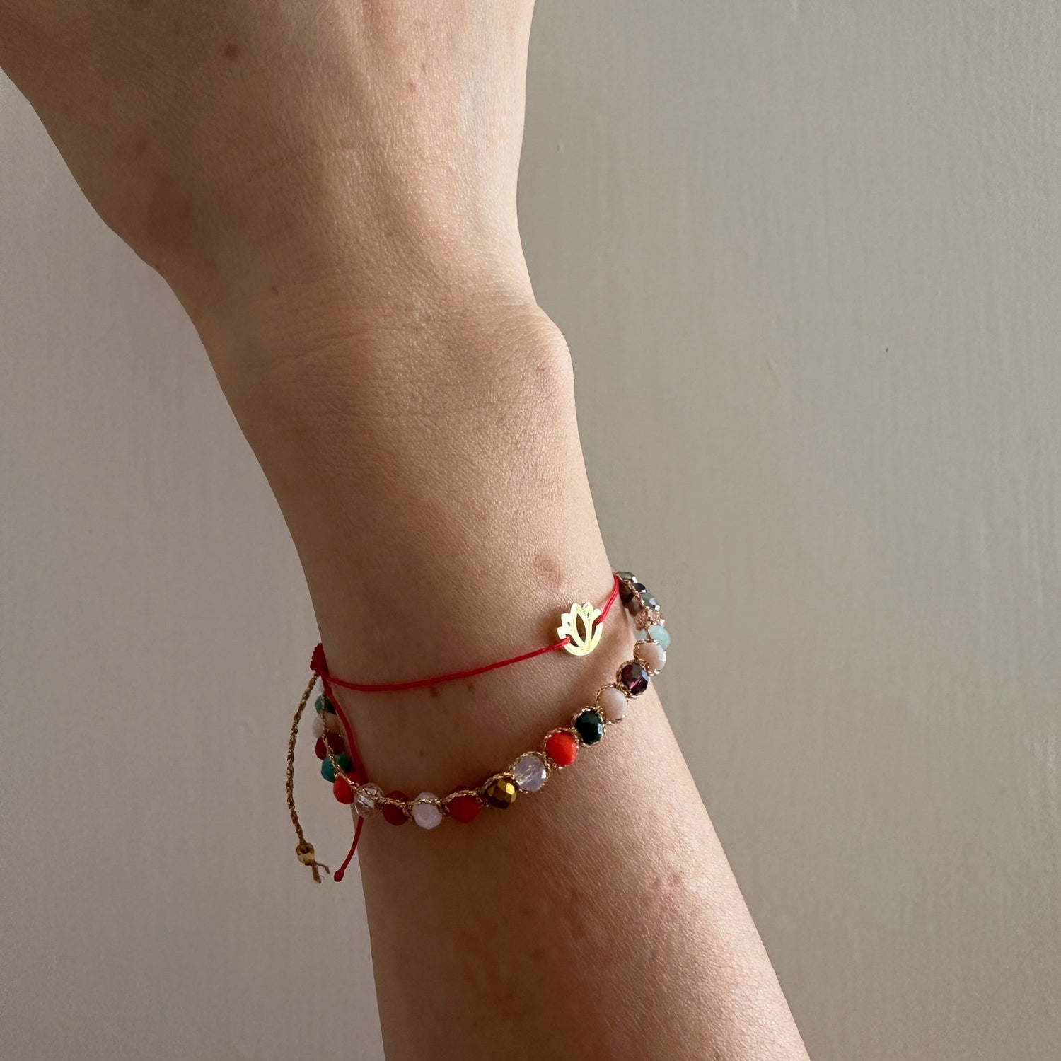 Wrist wearing a red cord gold charm bracelet with a beaded bracelet